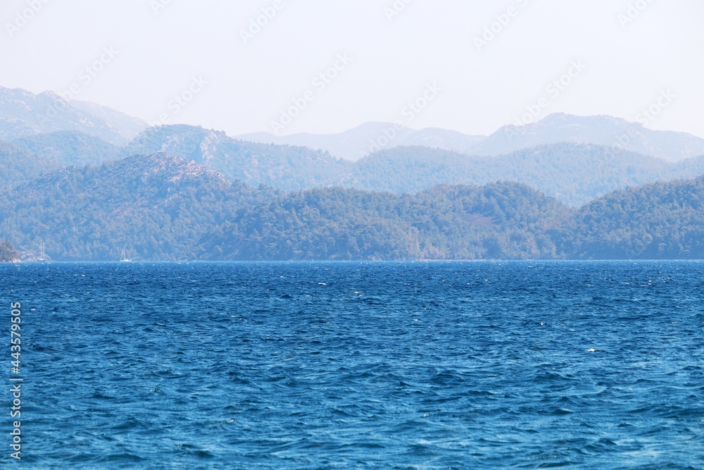 Obraz premium Scenic view to azure sea water and misty mountains covered with forest. Beach vacation, background for summer travel