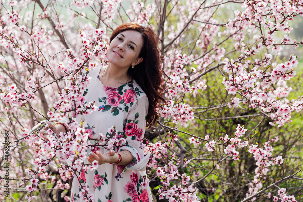 Beautiful brunette woman in a dress with flowers walks through the flowering garden in spring Beautiful brunette woman in a dress with flowers walks through the flowering garden in spring
