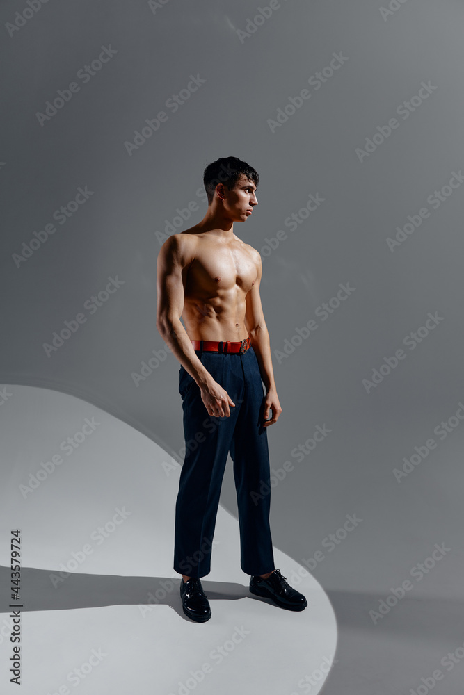 a handsome man with a naked torso in jeans and shoes stands on a gray background in full growth a handsome man with a naked torso in jeans and shoes stands on a gray background in full growth