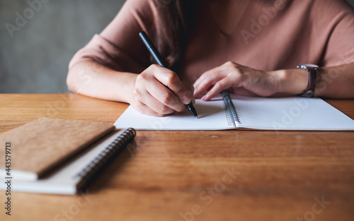 Closeup image of a woman writing on a blank notebook on wooden table
