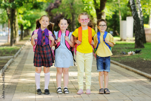 a group of school children in colored clothes with school bags and backpacks stands smiling against the background of greenery on the way to school. School year, back to school, knowledge day.