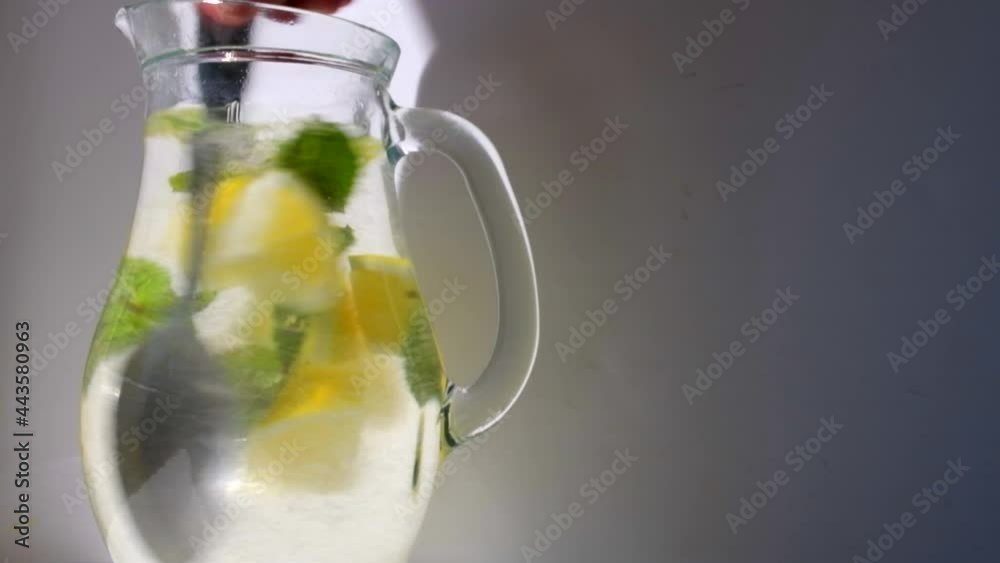 4K: Slow motion: when cooled, a drink called lemonade is mixed with a spoon in a glass decanter: lemon, mint and water in the rays of the summer sun from thirst 4K: Slow motion: when cooled, a drink called lemonade is mixed with a spoon in a glass decanter: lemon, mint and water in the rays of the summer sun from thirst