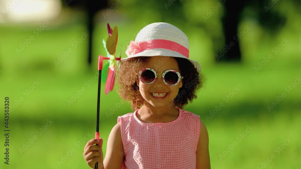 happy Black girl with blowing windmill. Cute little child holding colorful toy pinwheels on summer day in summer in nature happy Black girl with blowing windmill. Cute little child holding colorful toy pinwheels on summer day in summer in nature