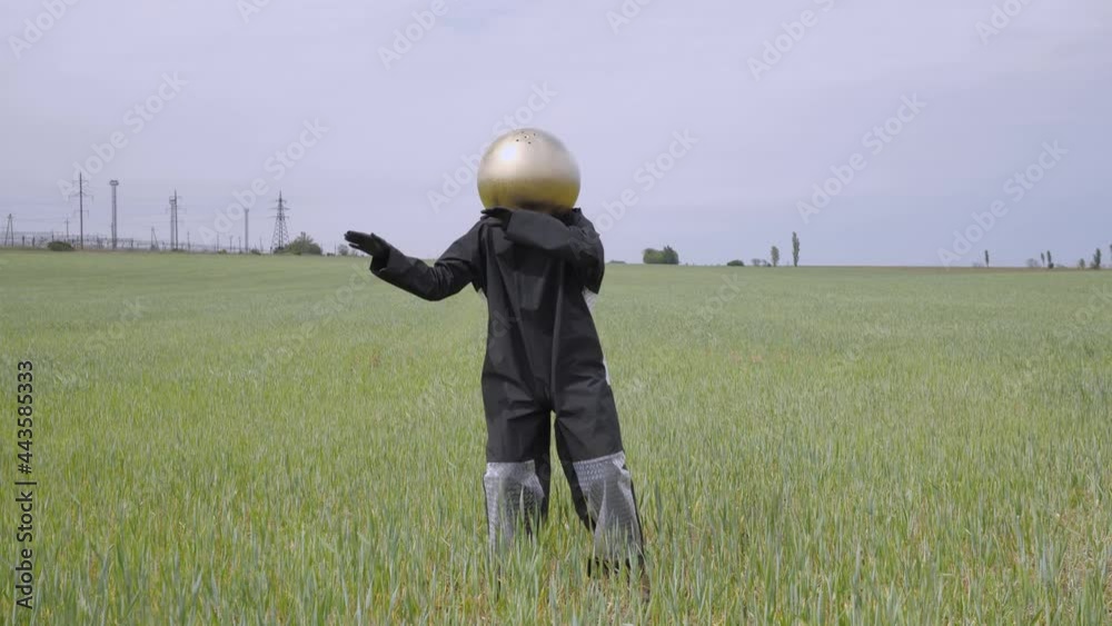 unknown person with a gold ball instead of a head in a black suit is standing on the black ground and dancing with his hands. field with vineyard and gray sky. transmission tower electricity pylon unknown person with a gold ball instead of a head in a black suit is standing on the black ground and dancing with his hands. field with vineyard and gray sky. transmission tower electricity pylon