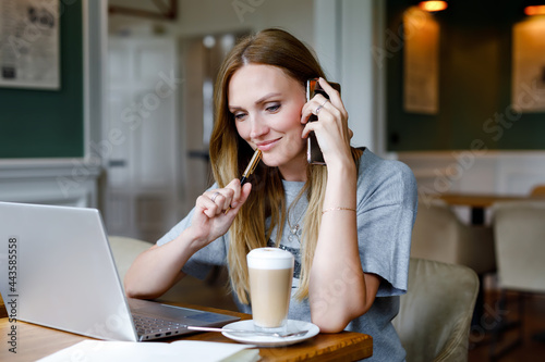 Portrait of young woman using technology of smartphone and looking at laptop. Young woman freelancer using laptop computer working in restaurant or hipster indoor cafe with coffee. Home office concept