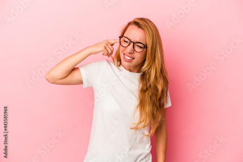 Caucasian blonde woman isolated on pink background covering ears with hands.