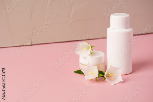 Set of cosmetic products with wild plants on pink background