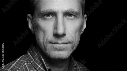 Mid aged wrinkled man portrait close up isolated against black background. Male with serious facial expression