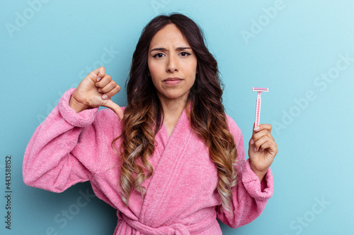 Young mexican woman wearing a bathrobe holding a knife isolated on blue background showing a dislike gesture  thumbs down. Disagreement concept.