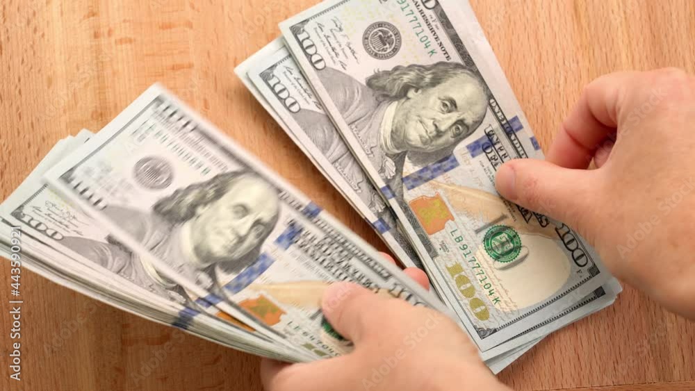 Woman's hands counting one hundred dollar bill on a wooden table, close-up Woman's hands counting one hundred dollar bill on a wooden table, close-up