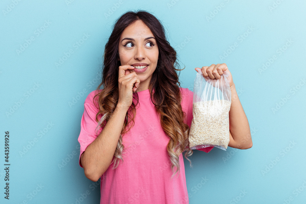 Young mixed race woman holding oatmeal isolated on blue background relaxed thinking about something looking at a copy space. Young mixed race woman holding oatmeal isolated on blue background relaxed thinking about something looking at a copy space.