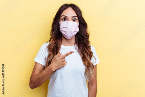 Young mixed race woman wearing a protection for virus isolated on yellow background Young mixed race woman wearing a protection for virus isolated on yellow background pointing to the side