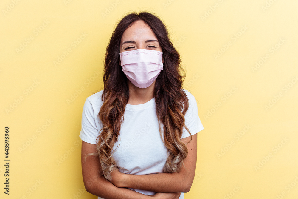 Young mixed race woman wearing a protection for virus isolated on yellow background laughing and having fun. Young mixed race woman wearing a protection for virus isolated on yellow background laughing and having fun.