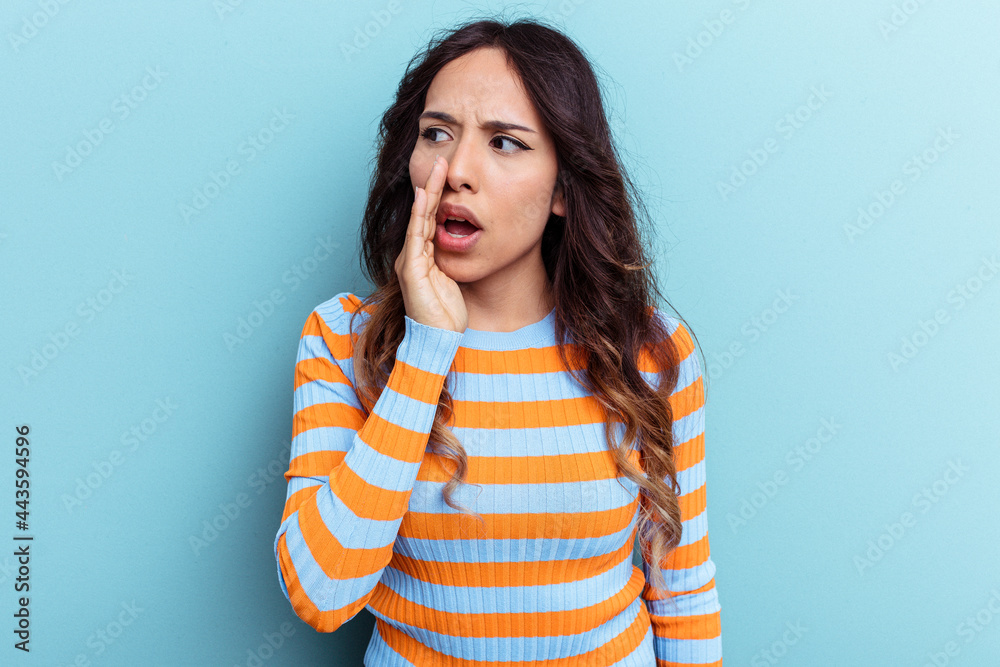Young mexican woman isolated on blue background is saying a secret hot braking news and looking aside Young mexican woman isolated on blue background is saying a secret hot braking news and looking aside