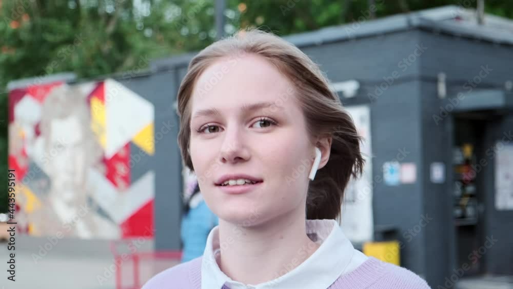 Young woman with short fair hair and white wireless headphones walks along local city street and dances on sunny day close view. Vlogger influncer street urban creative lifestyle concept. Young woman with short fair hair and white wireless headphones walks along local city street and dances on sunny day close view. Vlogger influncer street urban creative lifestyle concept.