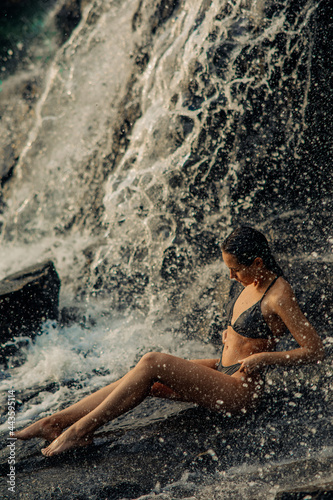 Woman sits under the waterfall and enjoys the falling water.