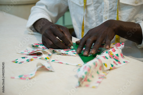 Unrecognizable tailor drawing outline on a fabric in his sewing shop. African man working in a workshop.
