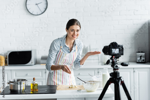 cheerful culinary blogger pointing with hand near dough and blurred digital camera. photo