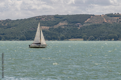 A white sailboat sails on wind-rippled water on Lake Trasimeno near Passignano, Italy