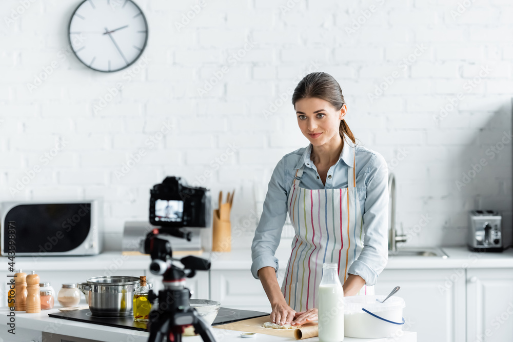 culinary blogger making dough in front of blurred digital camera in kitchen.
