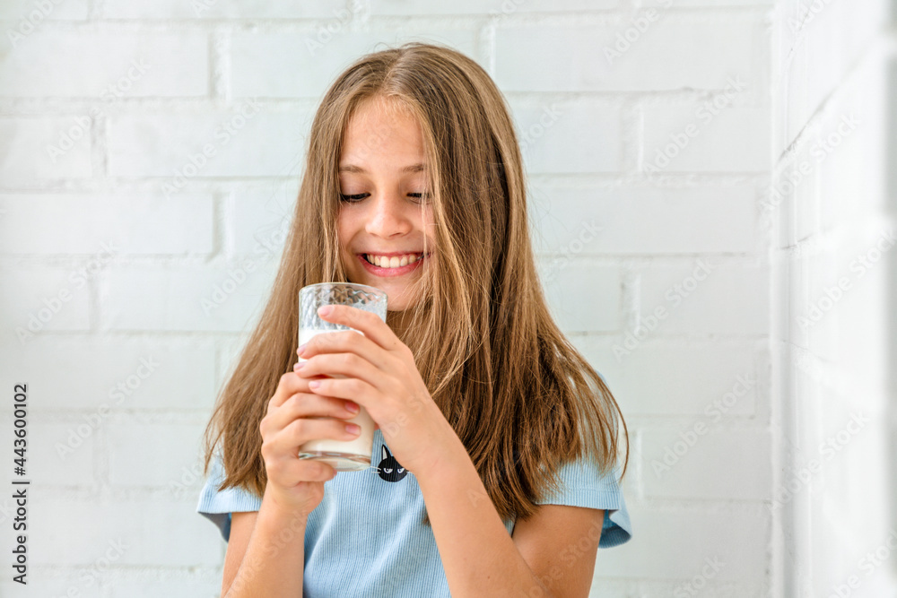 A beautiful little girl is having fun drinking a glass of fresh milk against a white brick wall A beautiful little girl is having fun drinking a glass of fresh milk against a white brick wall