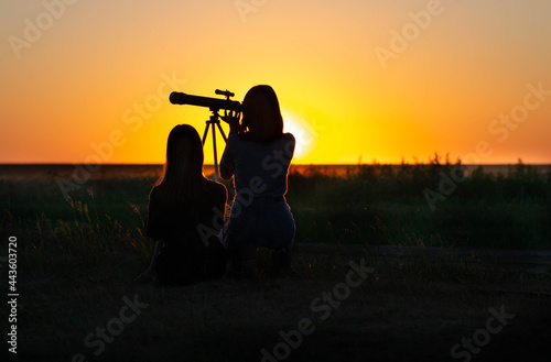 Girls at sunset in a field looking through a telescope