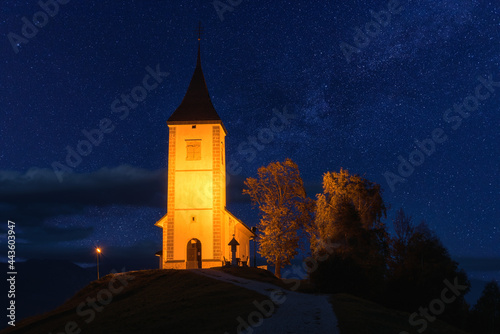 Scenic view of illuminated Jamnik church St Primus and Felician on the hill at night, Slovenia. Beautiful landscape with blue starry sky, outdoor travel background, famous tourist attraction