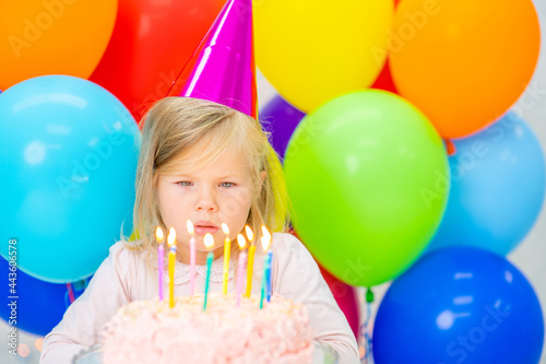 Happy girl wearing party's cap blowing candles on birthday cake. Empty space for text