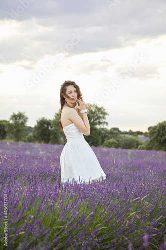  American shot of a young woman in white dress in the lavender fields of Brihuega, in Spain. He is posing among plants, while walking.