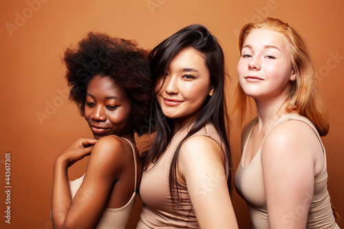 young pretty asian, caucasian, afro woman posing cheerful together on brown background, lifestyle diverse nationality people concept