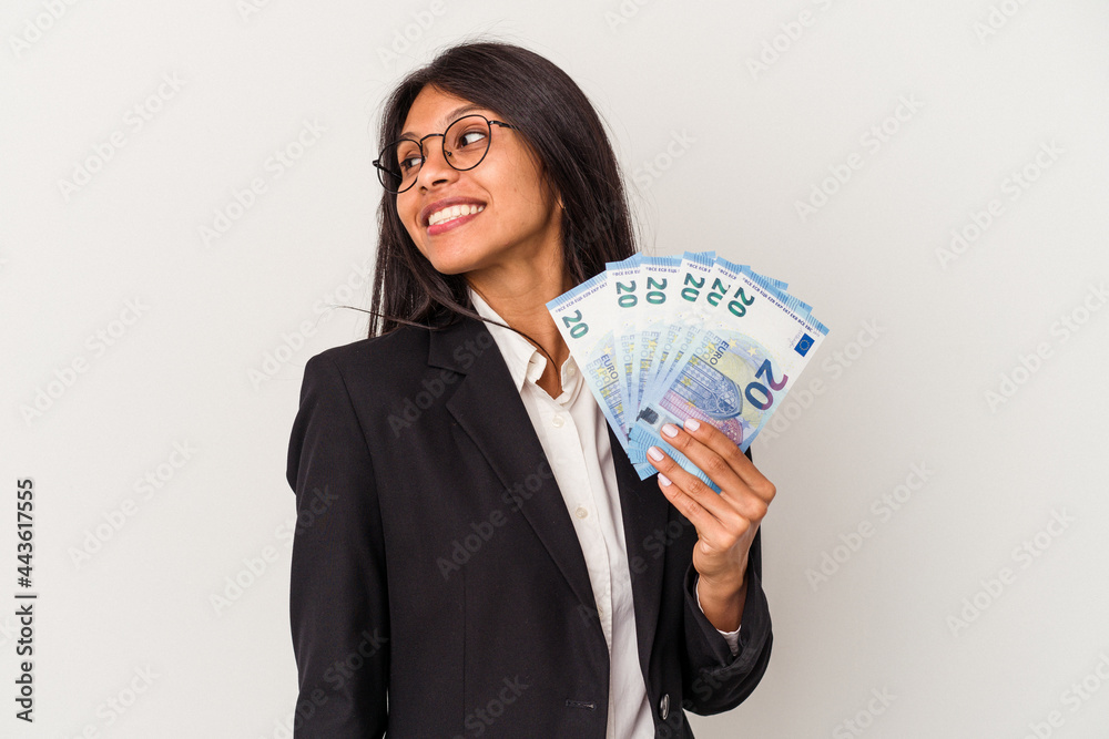 Young business latin woman holding bills isolated on white background looks aside smiling, cheerful and pleasant. Young business latin woman holding bills isolated on white background looks aside smiling, cheerful and pleasant.