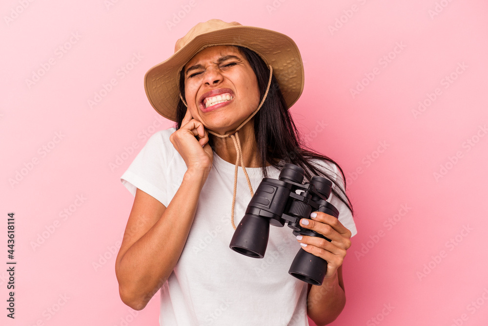 Young latin woman holding binoculars isolated on pink background covering ears with hands. Young latin woman holding binoculars isolated on pink background covering ears with hands.