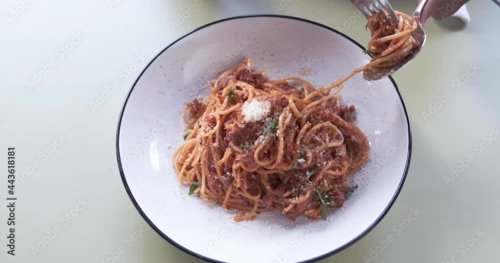 Close up of hands using spoon and fork to roll and eat spaghetti Bolognese