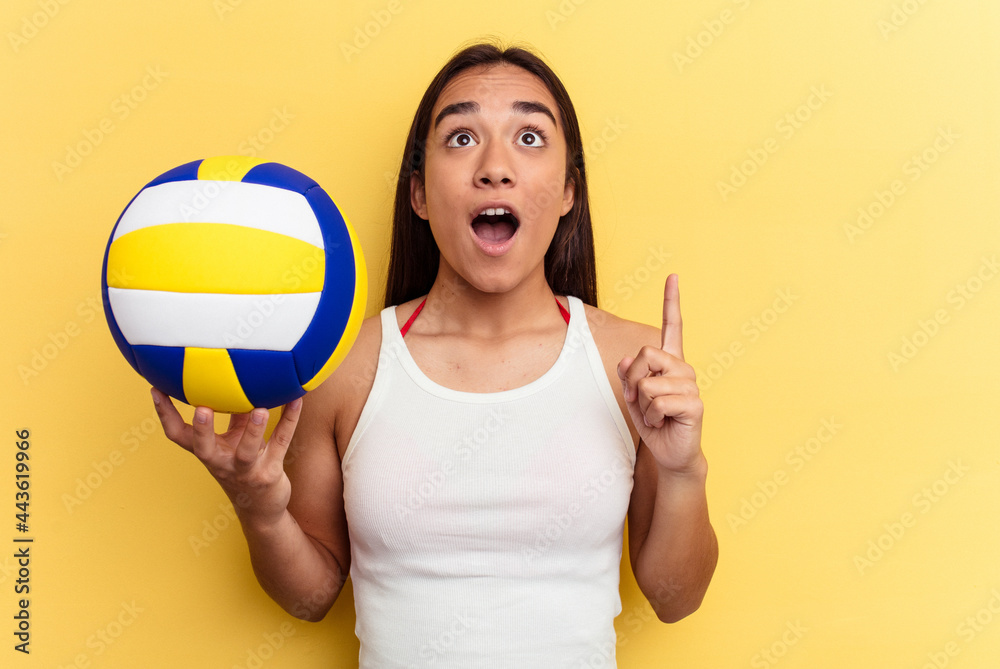 Young mixed race woman playing volleyball on the beach isolated on yellow background pointing upside with opened mouth. Young mixed race woman playing volleyball on the beach isolated on yellow background pointing upside with opened mouth.
