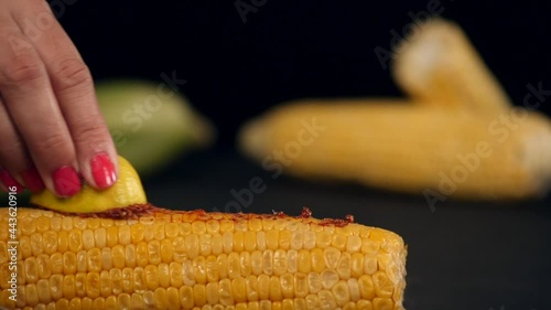 An Indian chef's hand applying lemon and Masala on a grilled Bhutta in the kitchen. Closeup shot of two maize kept on a wooden table against a blurred background photo