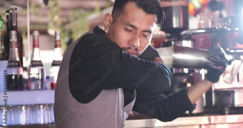 Expert asian bartender shaking cocktail at the bar using metal mixer over colorful background with alcoholic beverages Expert asian bartender shaking cocktail at the bar using metal mixer over colorful background with alcoholic beverages