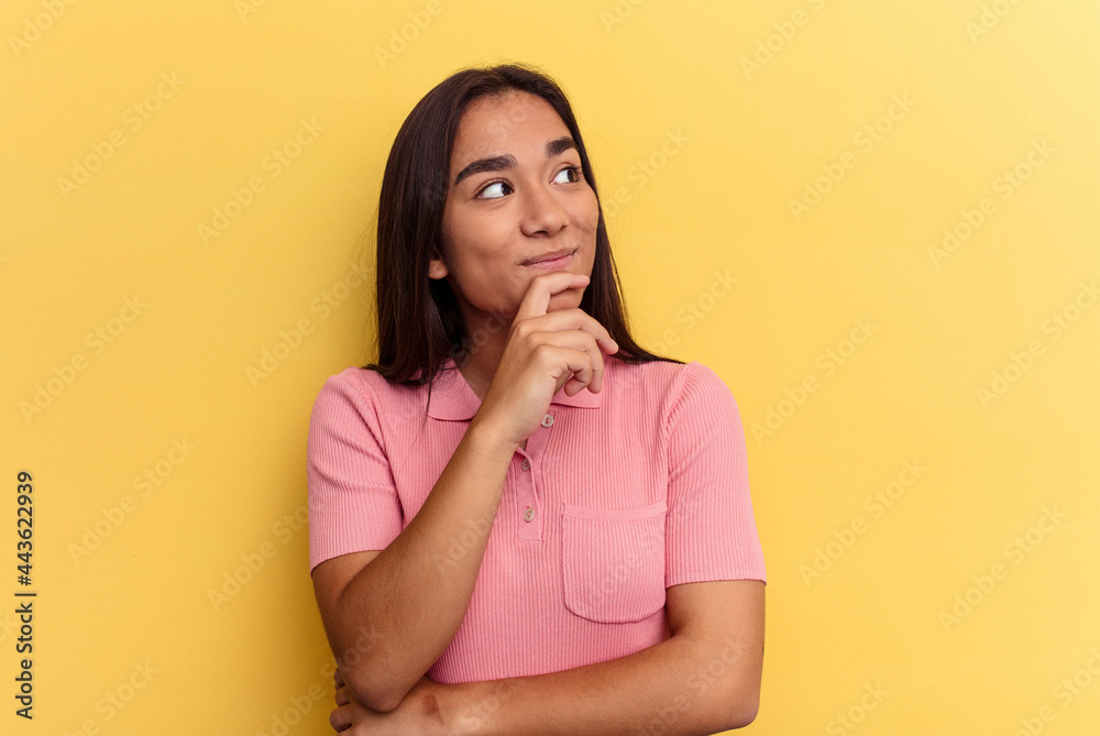 Young mixed race woman isolated on yellow background relaxed thinking about something looking at a copy space. Young mixed race woman isolated on yellow background relaxed thinking about something looking at a copy space.