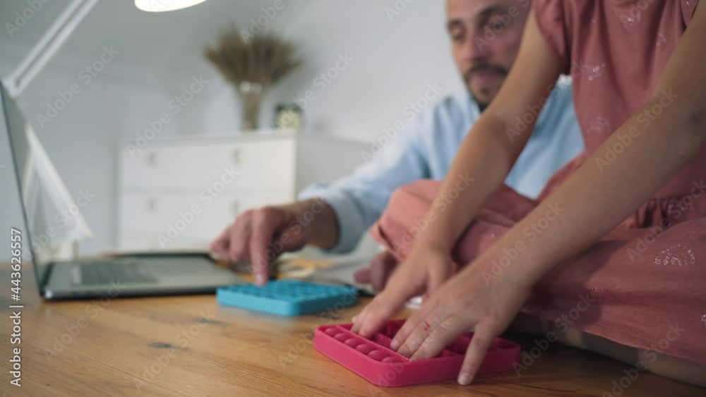 A man and a child are playing Poppit. A man working at a laptop takes a break and plays Poppit with a girl. An anti-stress toy. Popular trends of 2021. Self-isolation. Relax A man and a child are playing Poppit. A man working at a laptop takes a break and plays Poppit with a girl. An anti-stress toy. Popular trends of 2021. Self-isolation. Relax