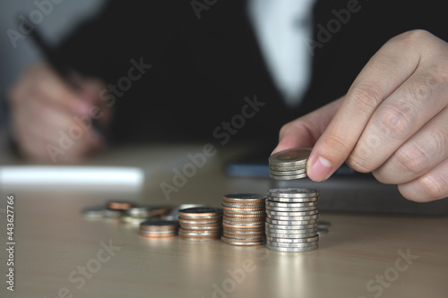 businessman laying a stack of silver coins with his hands and take note of the financial plan. Money saving or growing business planning concept