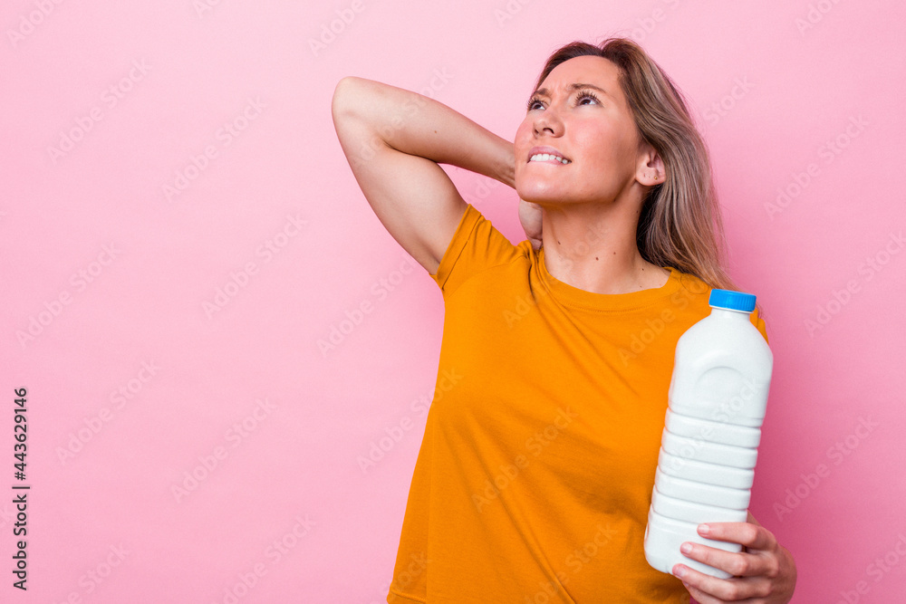 Young australian woman holding a bottle of milk isolated on pink background touching back of head, thinking and making a choice. Young australian woman holding a bottle of milk isolated on pink background touching back of head, thinking and making a choice.