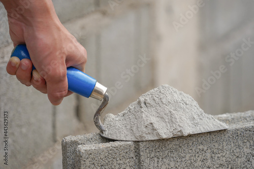 hand of industrial bricklayer hold aluminium trowel scoop mortar put on a brick block on construction site with copy space for text, selective focus photo
