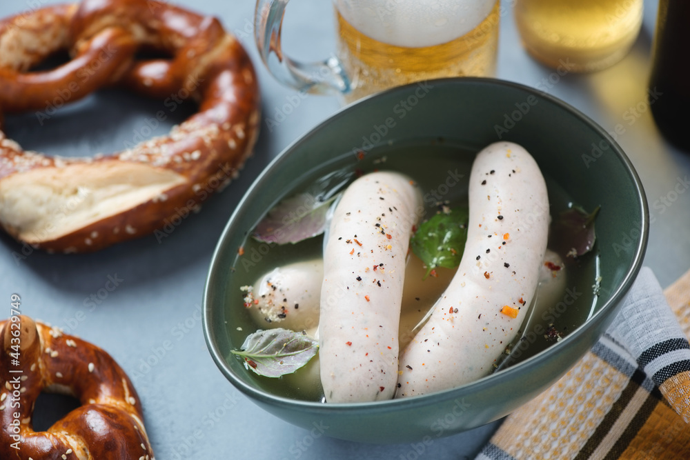 Bowl with munich sausages served in a broth with pretzels and beer, studio shot on a grey concrete background, selective focus Bowl with munich sausages served in a broth with pretzels and beer, studio shot on a grey concrete background, selective focus