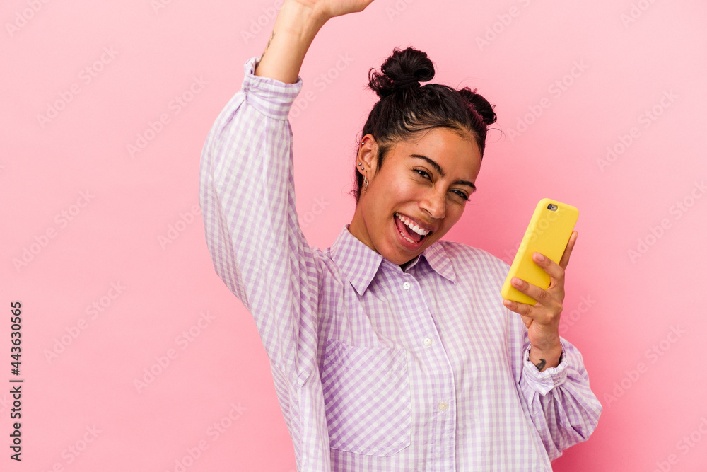 Young latin woman holding a mobile phone isolated on pink background raising fist after a victory, winner concept. Young latin woman holding a mobile phone isolated on pink background raising fist after a victory, winner concept.