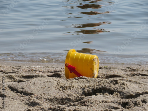 a yellow baby bucket lies sideways in the sand on the river bank
