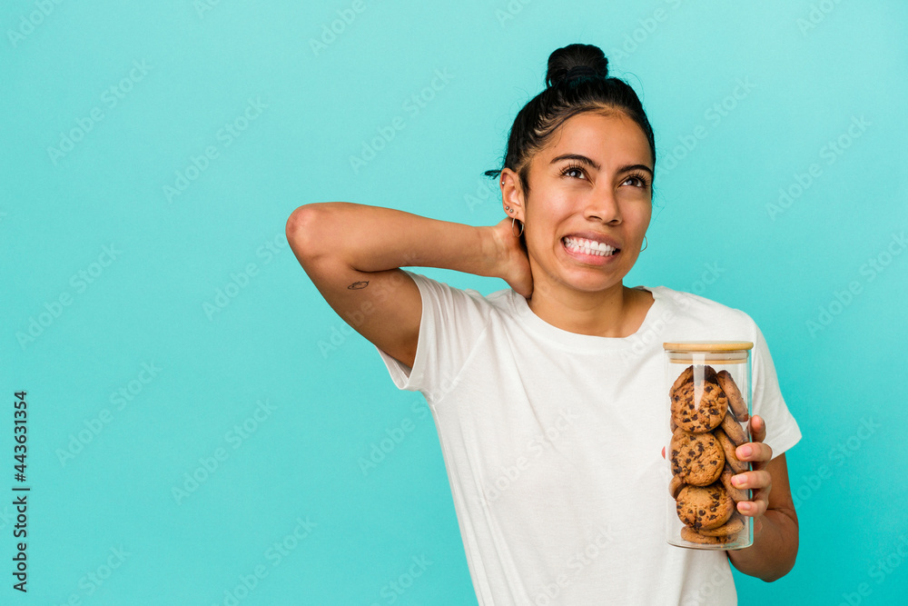 Young latin woman holding a cookies jar isolated on blue background touching back of head, thinking and making a choice. Young latin woman holding a cookies jar isolated on blue background touching back of head, thinking and making a choice.