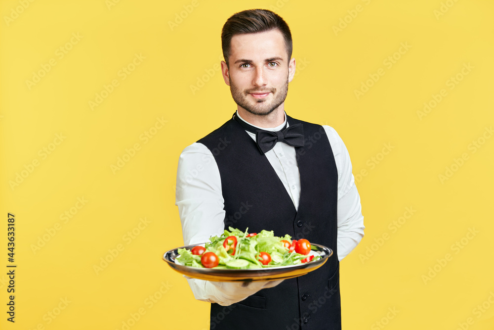 Happy smiling waiter holding plate with healthy vegetable salad ready to serve