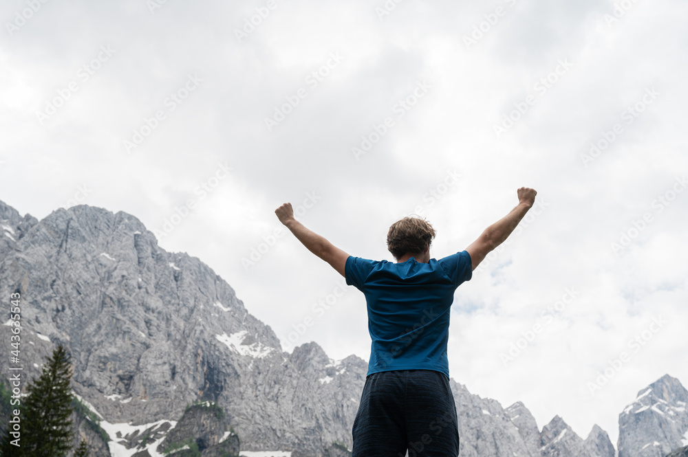 Young man standing victorious with his arms raised high surrounded with mountains