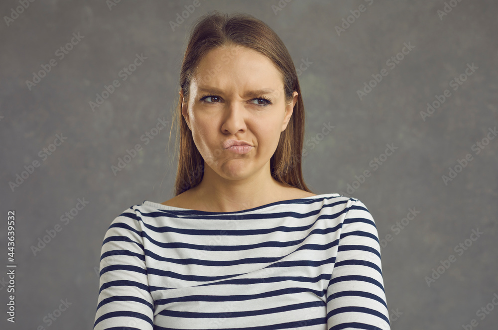 Studio close up portrait of displeased grumpy mad beautiful young woman pouting lips and looking away with funny expression of displeasure and resentment on face Studio close up portrait of displeased grumpy mad beautiful young woman pouting lips and looking away with funny expression of displeasure and resentment on face