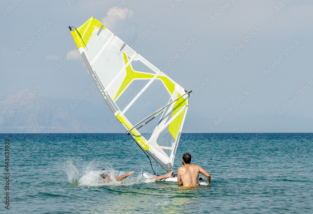 Naklejka premium Man Fell from a Windsurfing Board in the Sea. Summer Water Sport Activities in Greece. Horizon Line in Background. Surf Teacher is Watching and Helping