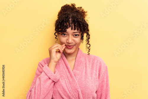 Young mixed race woman wearing a pink bathrobe isolated on pink background with fingers on lips keeping a secret.